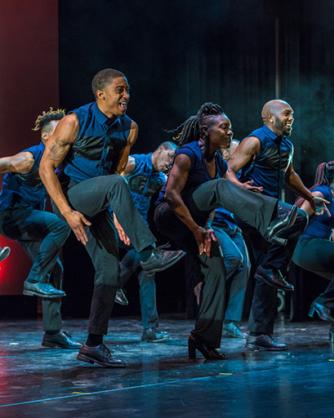 Dance members of Step Africa!, clapping under their lifted legs on a stage with blue and red lighting