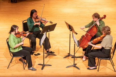 four female students on stage playing string instruments