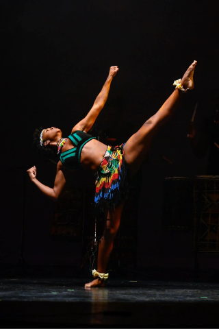 Step Africa! dancer posing with arm and leg extended on a dark stage