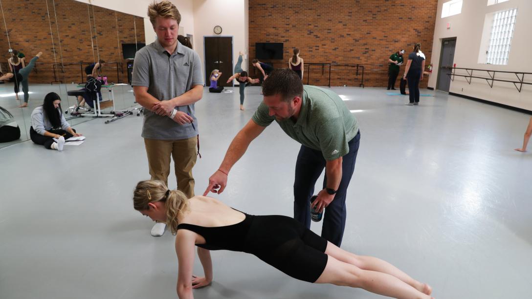 a student and professor examine a dancer as they are in a plank