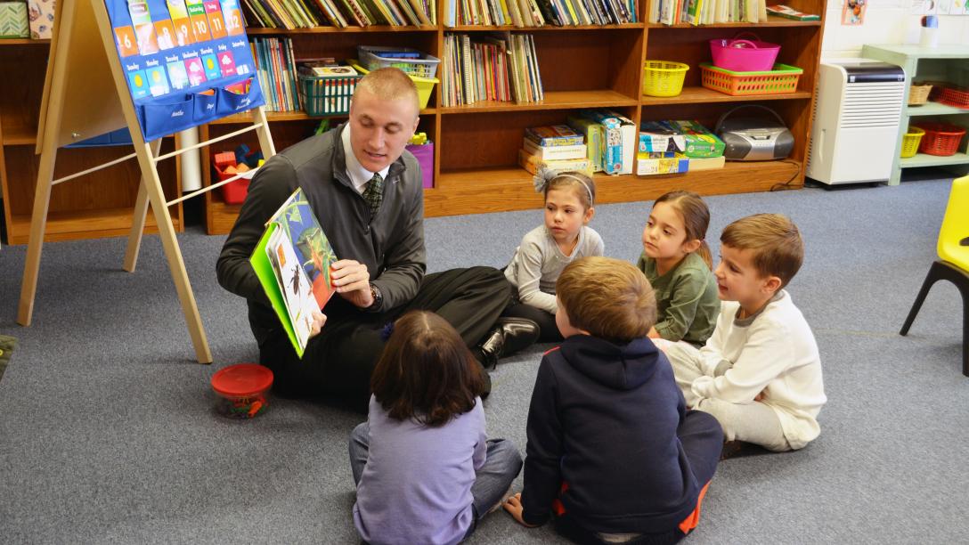 a male student teacher reads to children