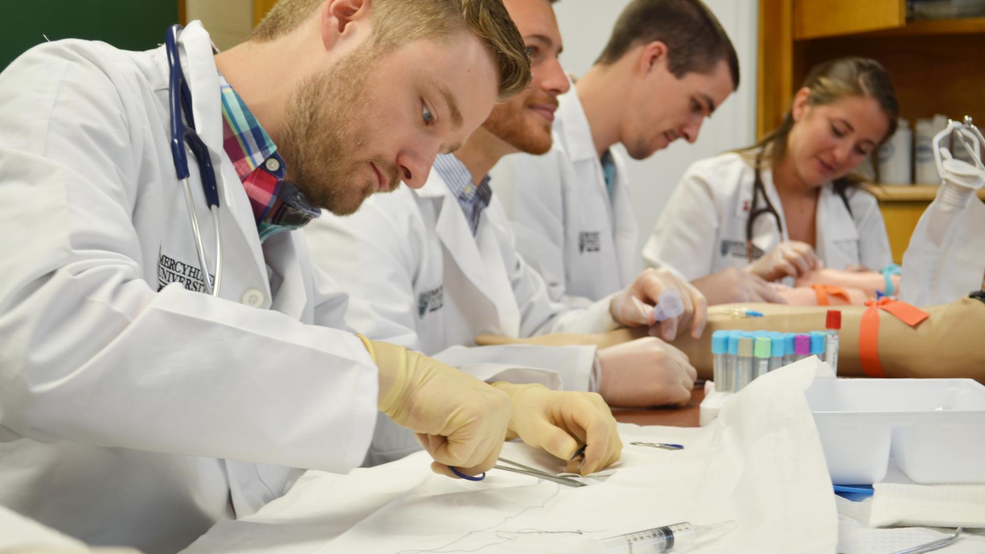 three male physician assistant students and one female student work in a lab