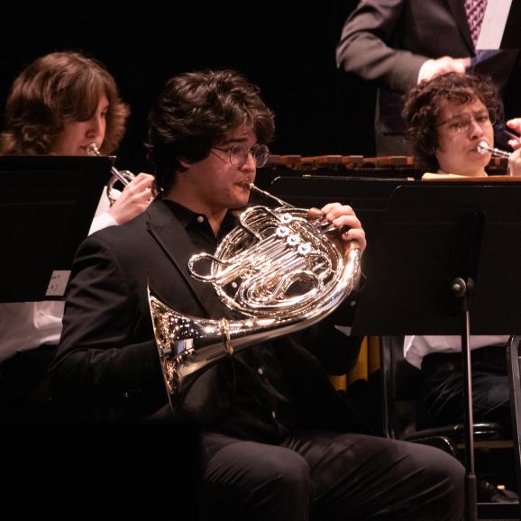 a male student playing french horn in an orchestra