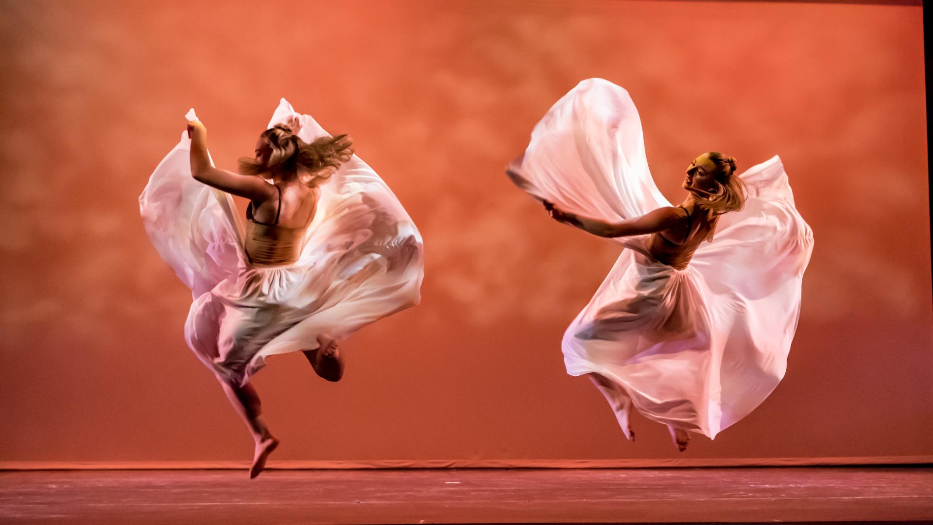 two female dancers jump with flowing white costumes