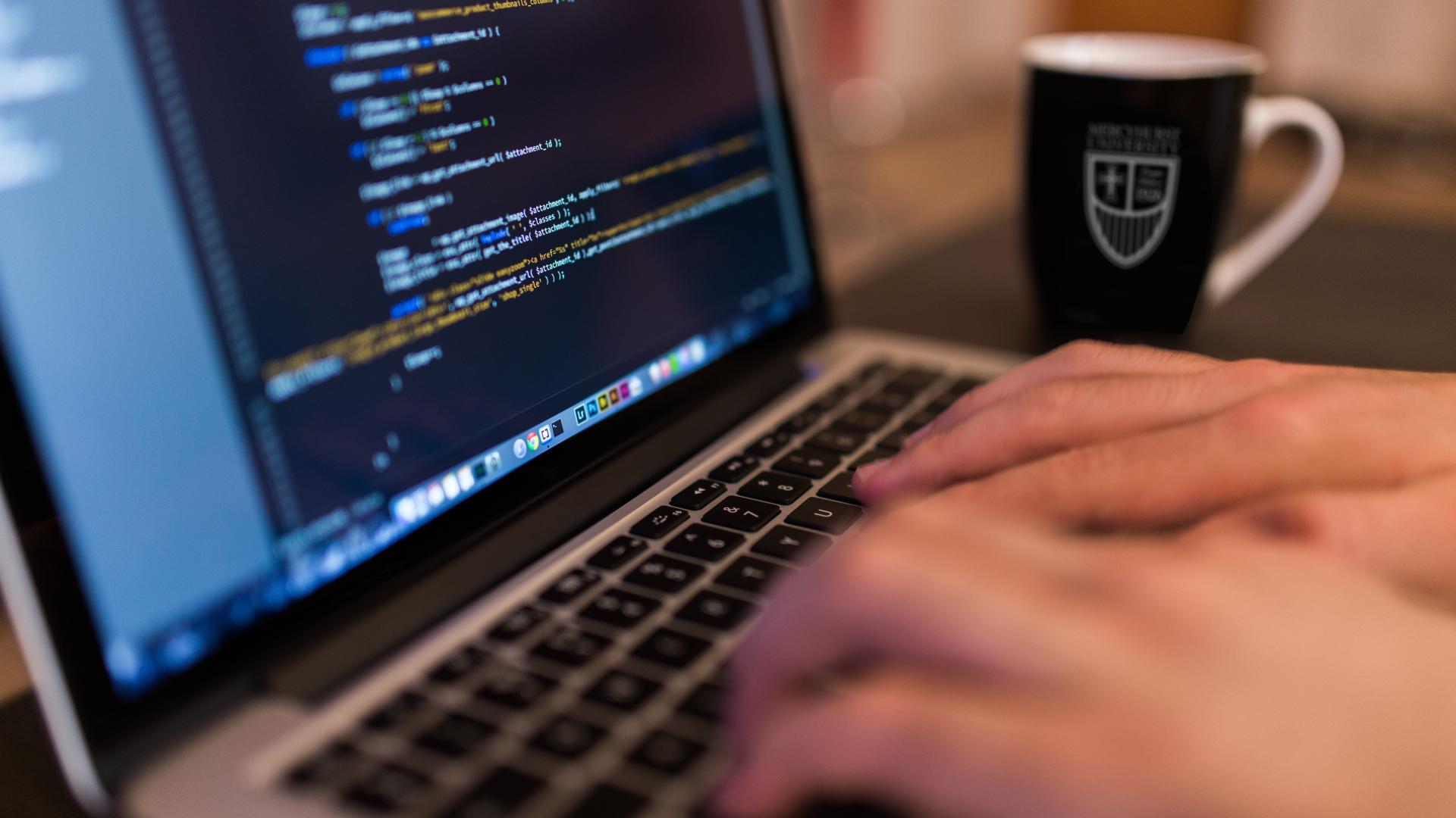 closeup of a laptop and hands with a mug in the background