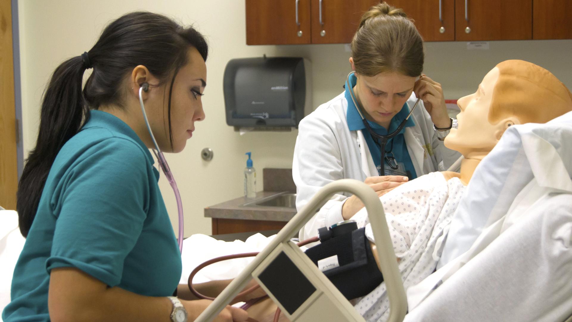 Two nursing students checking vitals on practice mannequin.