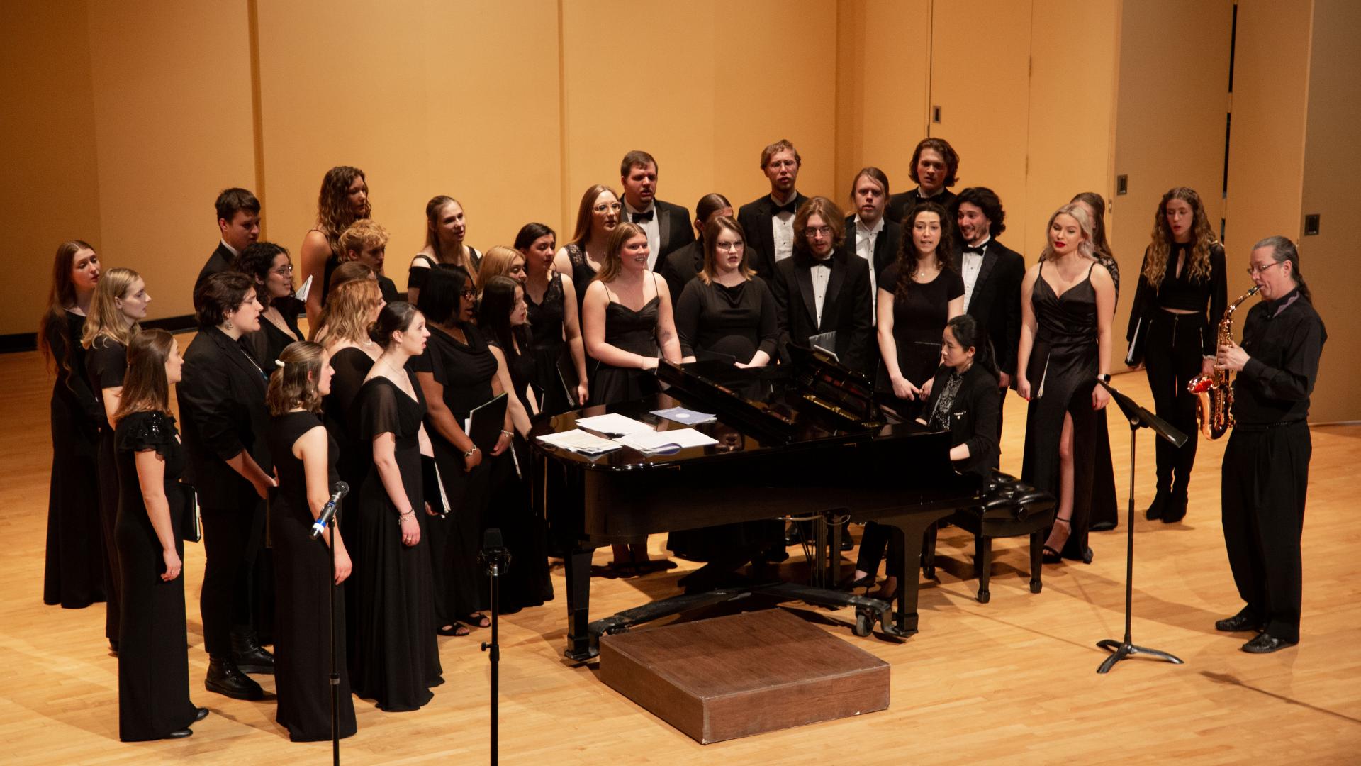 mercyhurst concert choir sings around a grand piano on stage