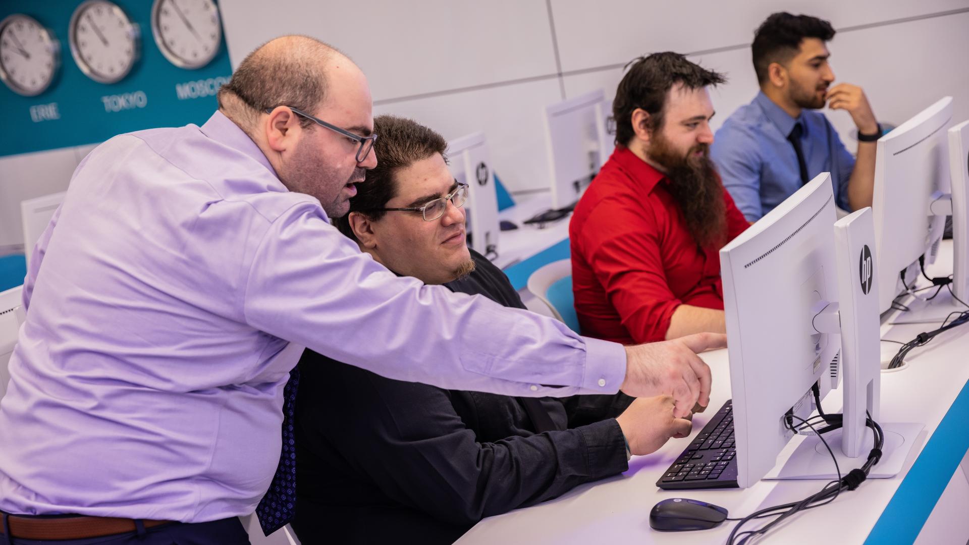 professor pointing at students computer in cyber lab