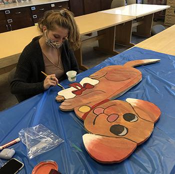 Student painting a puppy on wood