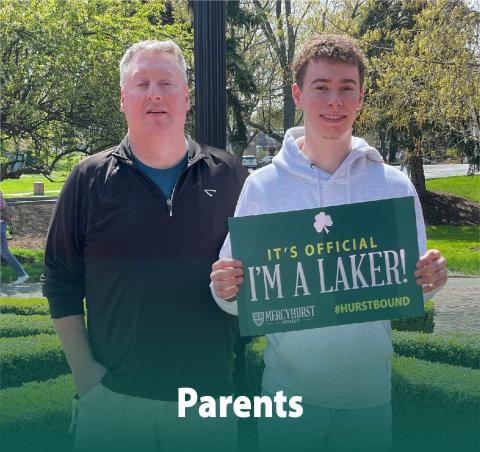 A dad posing with his son who has decided to attend Mercyhurst. The son holds a poster reading "It's Official. I'm a Laker!"