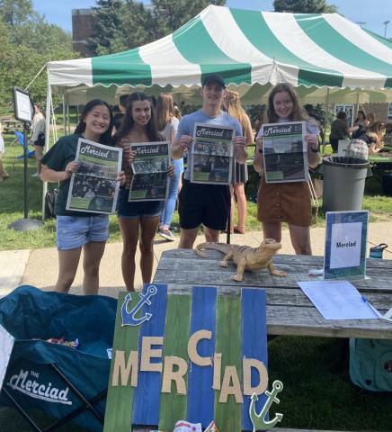 Students holding Merciad newspaper outside at a booth