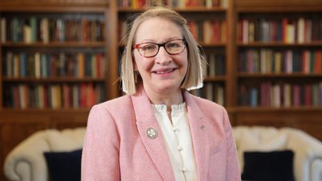 Image of President Getz smiling and standing in front of a couch and bookshelf