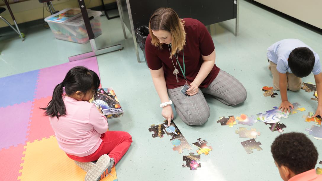a female student teacher builds a puzzle with children