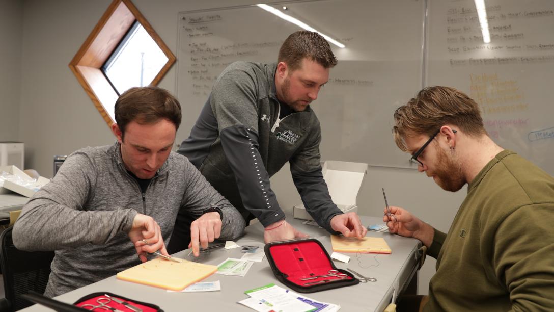 two students and professor learn how to use sutures