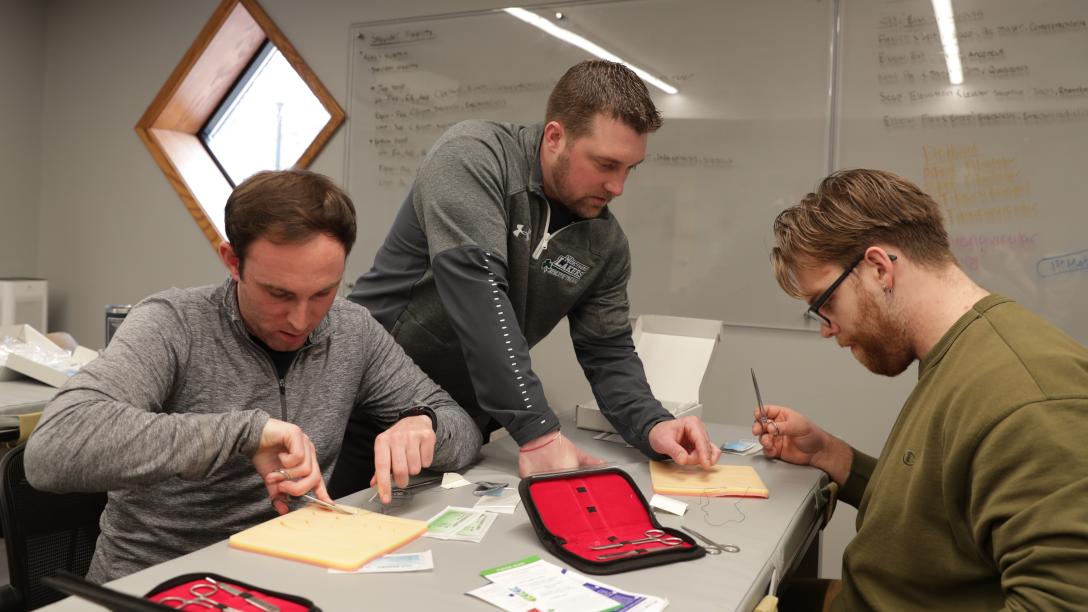 two students and professor learn how to use sutures