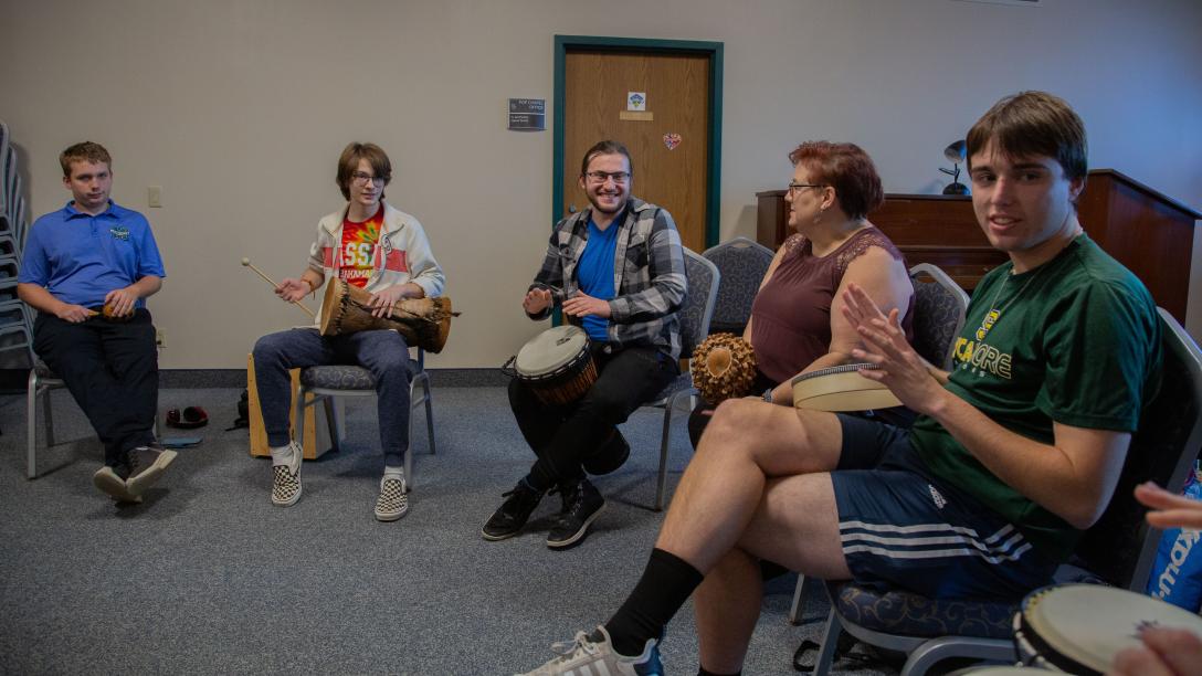 Five Music Therapy students playing percussion instruments sitting down in a classroom setting