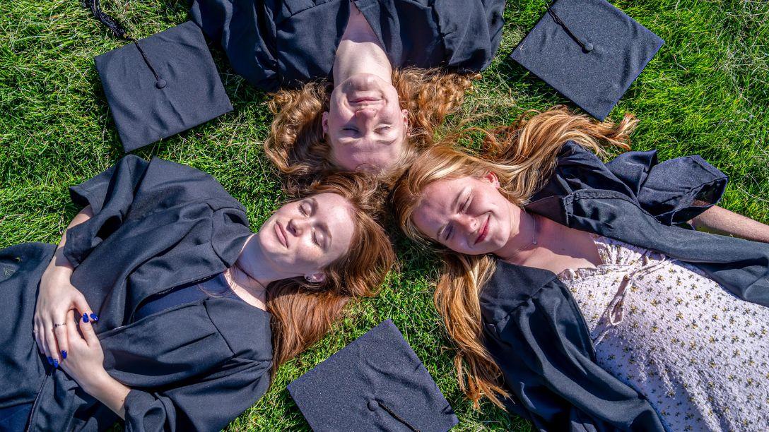 Graduation 2026 three female graduates laying on campus lawn
