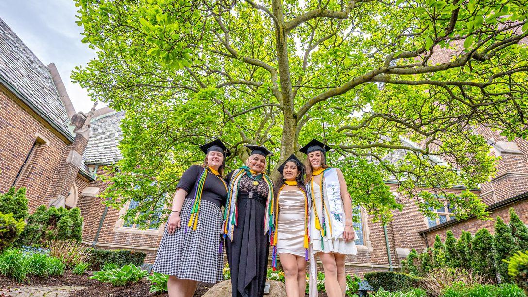 Graduation 2026 four female graduates in front of Christ the King Chapel and magnolia tree