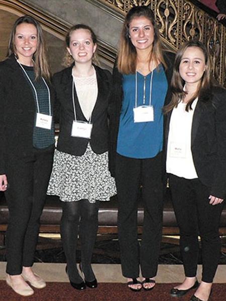 Four female Human Resource Management students posing for a photo in conference badges